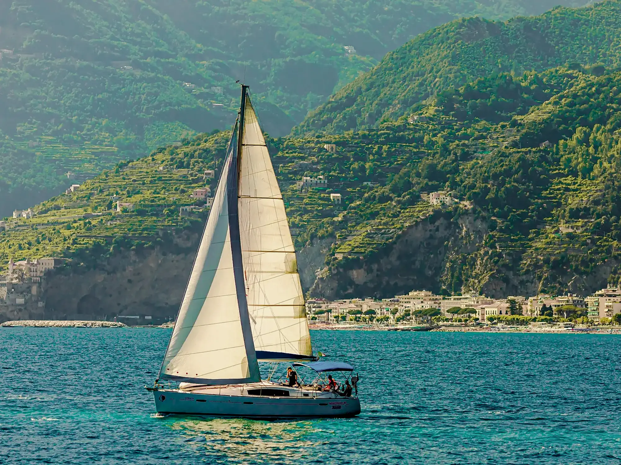 Sailing boat in front of green hills and coast. Amalfi, Campania, Italy.
