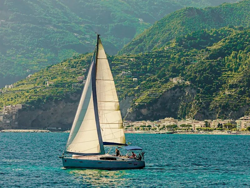 Sailing boat in front of green hills and coast. Amalfi, Campania, Italy.
