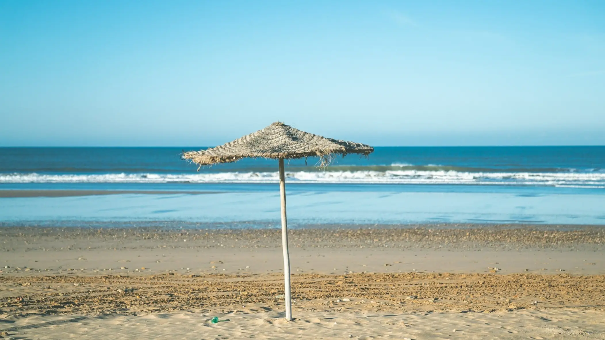 Marokko, Strand Ein Strandschirm am Strand von Sidi Bouzid, Marokko bei Sonnenschein und mit dem blauen Meer im Hintergrund.