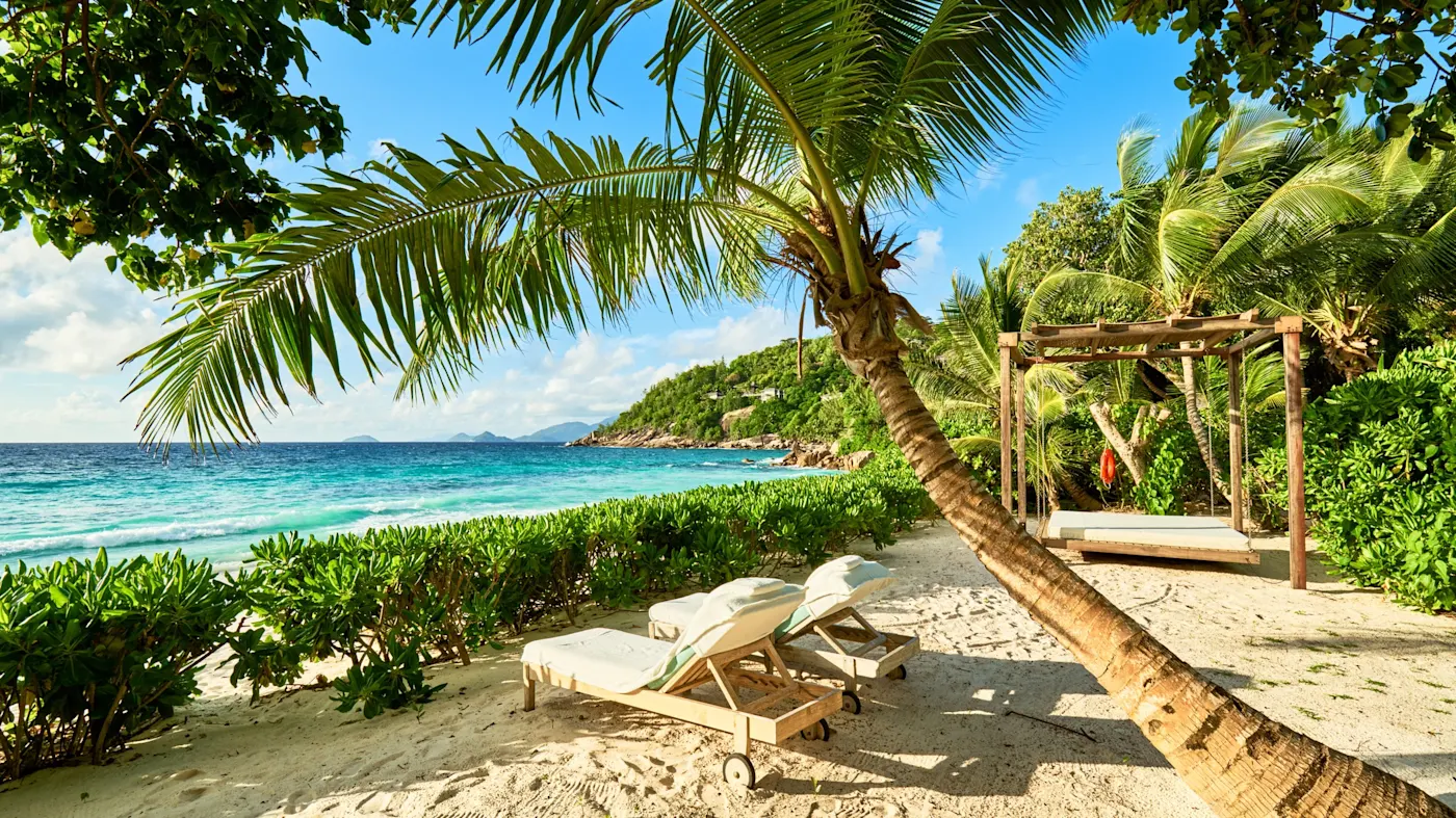 Strand, Mahé, Seychellen Holzstühle unter dem Schatten einer Palme an einem exotischen Strand mit Palmen, Seychellen