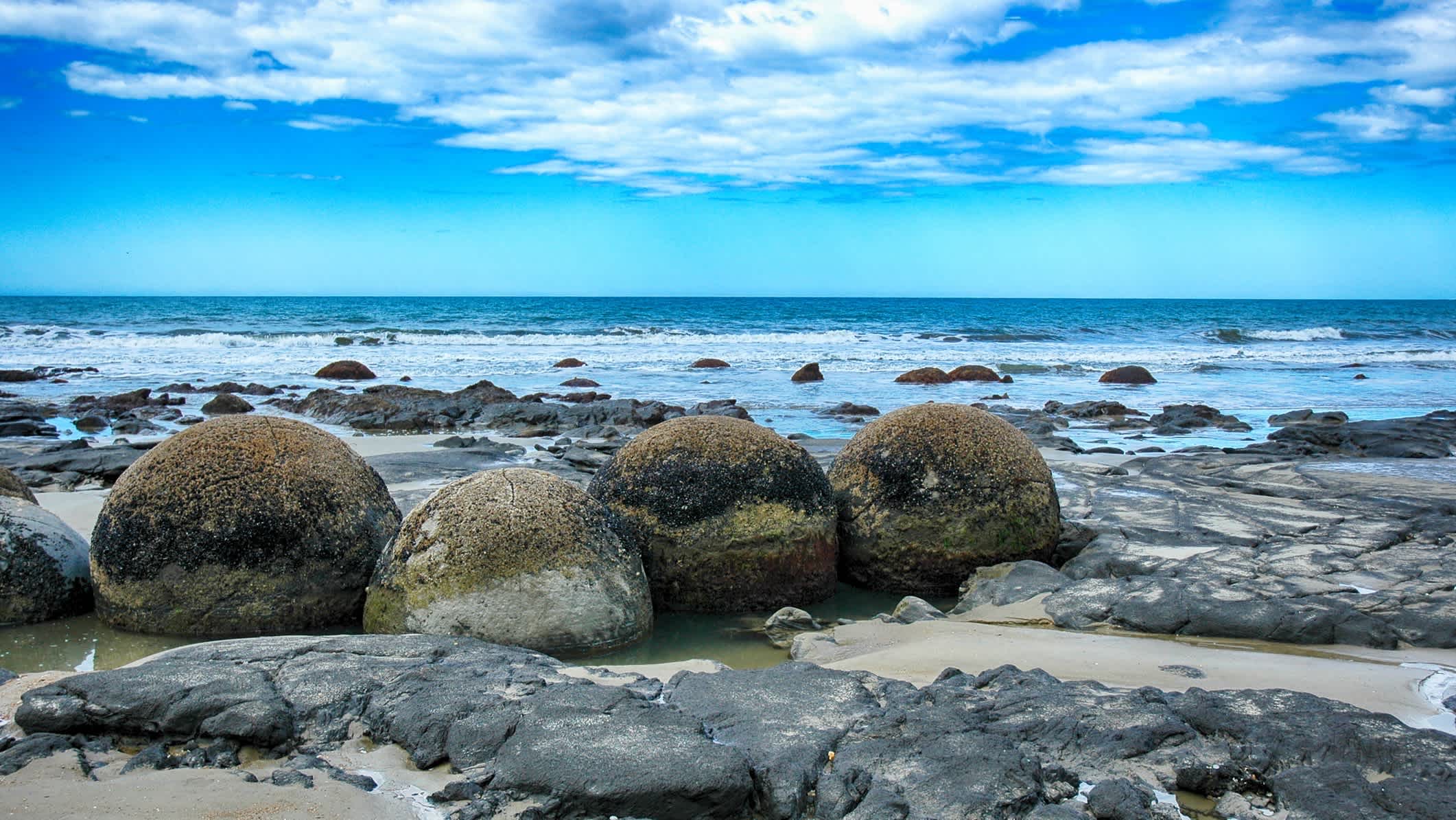 Der Strand Moeraki Boulders am Koekohe Beach in der Nähe von Oamaru, Neuseeland mit vielen Felsen im Bild und Blick auf das Wasser.