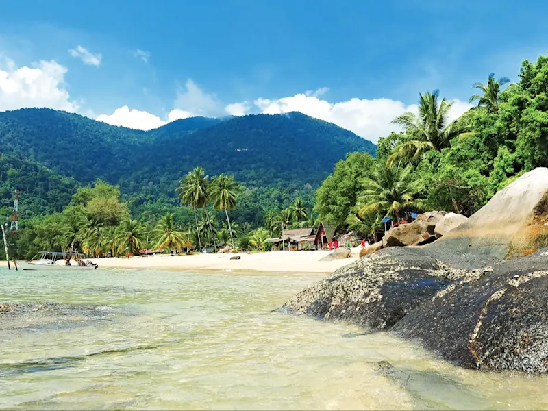 Sandstrand mit Palmen und Bergen im Hintergrund. Tioman-Insel, Pahang, Malaysia.