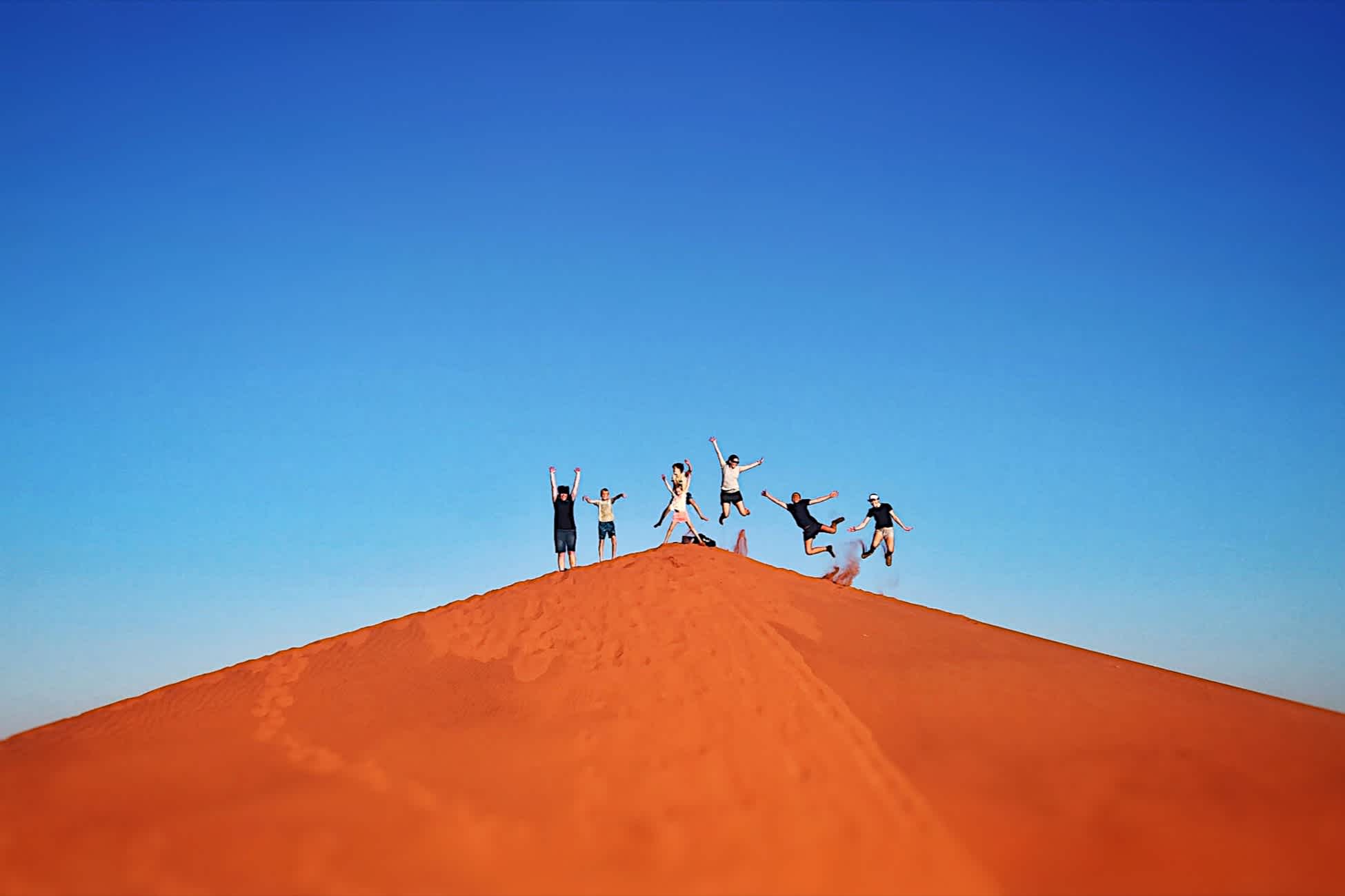 Eine Gruppe von Menschen springt auf einer Sanddüne in NamibRand, Namibia.
