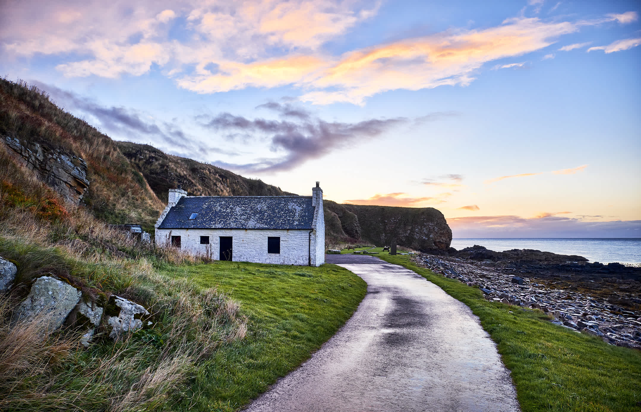 Ein Weg führt zu einem kleinen weißen Haus an der Küste Schottlands.