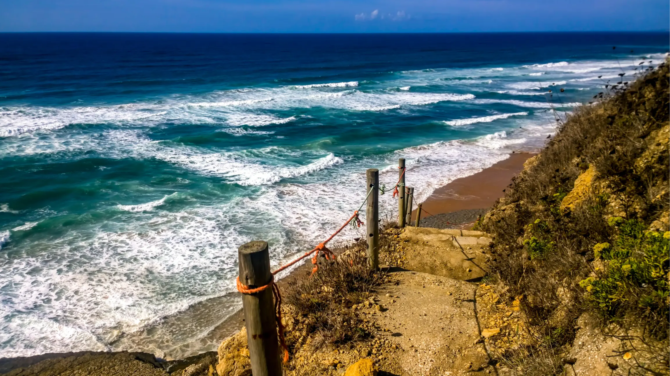 Der Strand Praia Da Aguda, Portugal mit Blick auf einen gesicherten Weg, der an der Klippe entlang führt und mit Aussicht auf das weite blaue Meer.