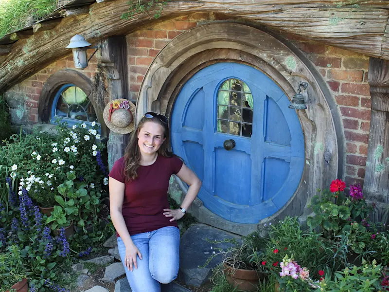 Neuseeland, Nordinsel, Matamata, Hobbit-Haus Eine Frau posiert vor einem Hobbit-Haus in der Hobbiton-Filmkulisse, Matamata, Nordinsel, Neuseeland.