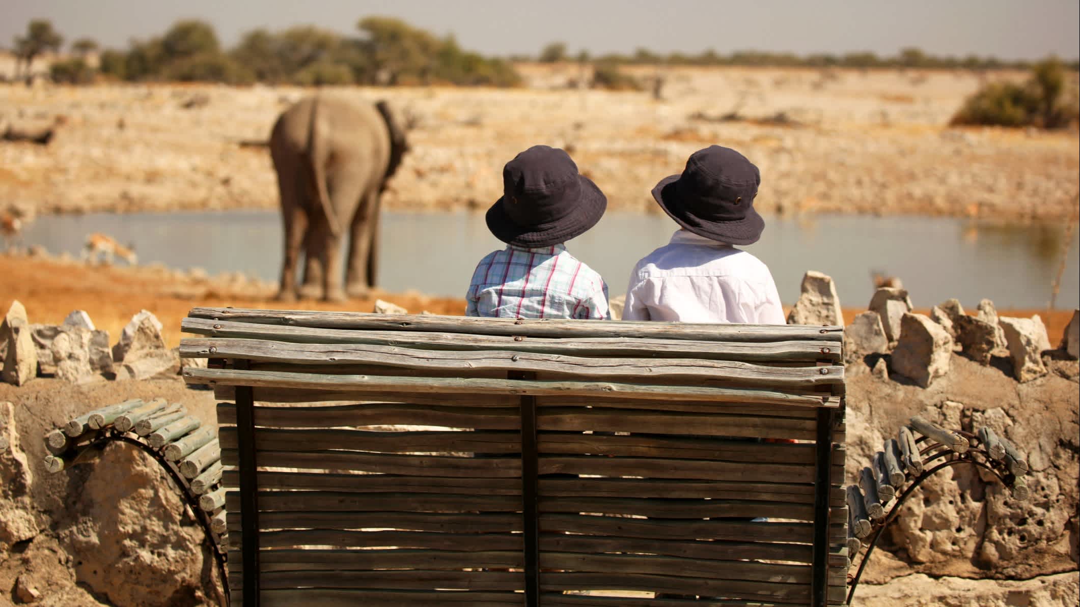 Kinder beobachten Elefanten im Wasserloch Okaukuejo im Etosha, Namibia.

