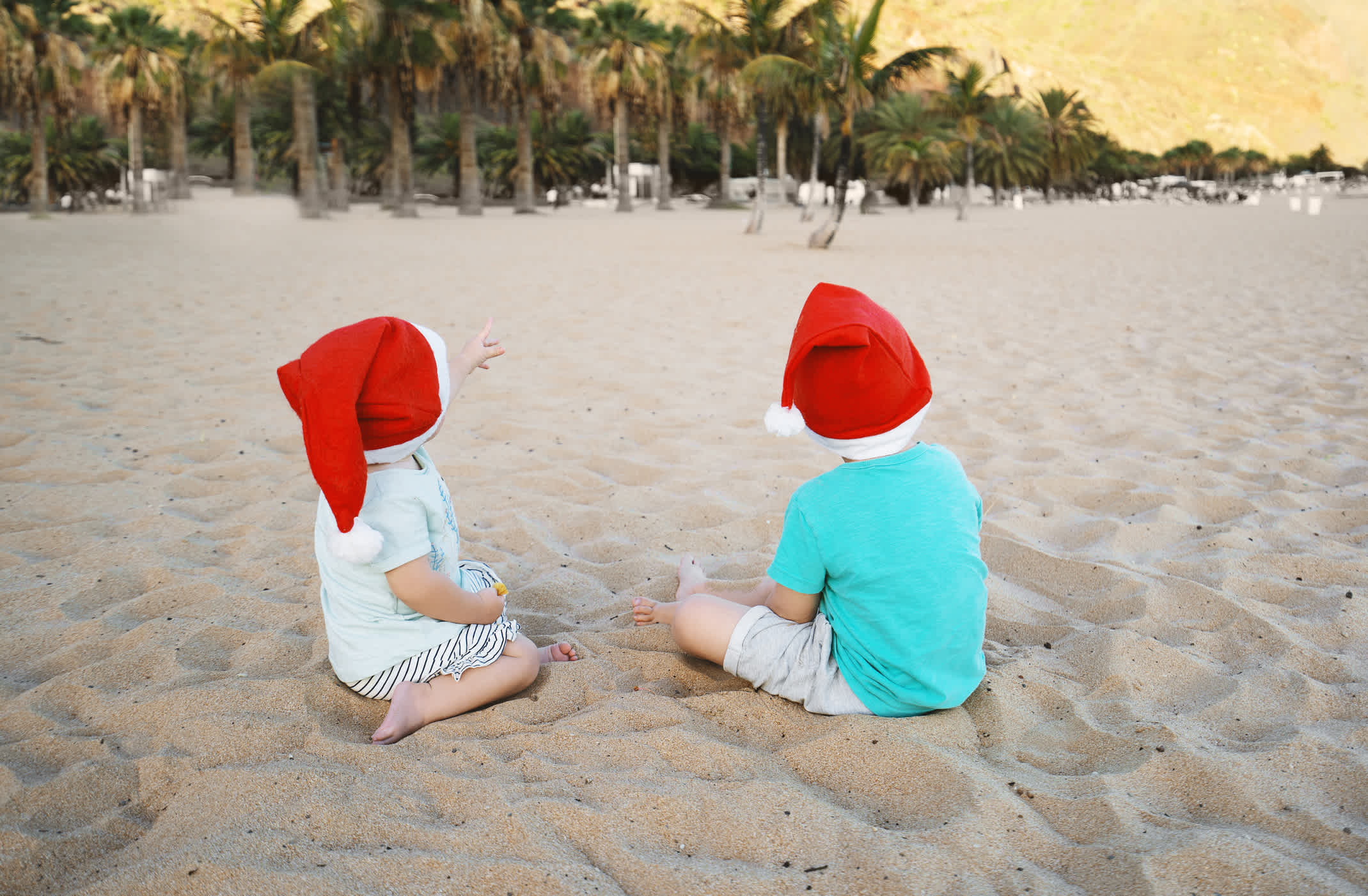 Zwei Kleinkinder mit Weihnachtsmütze am Strand