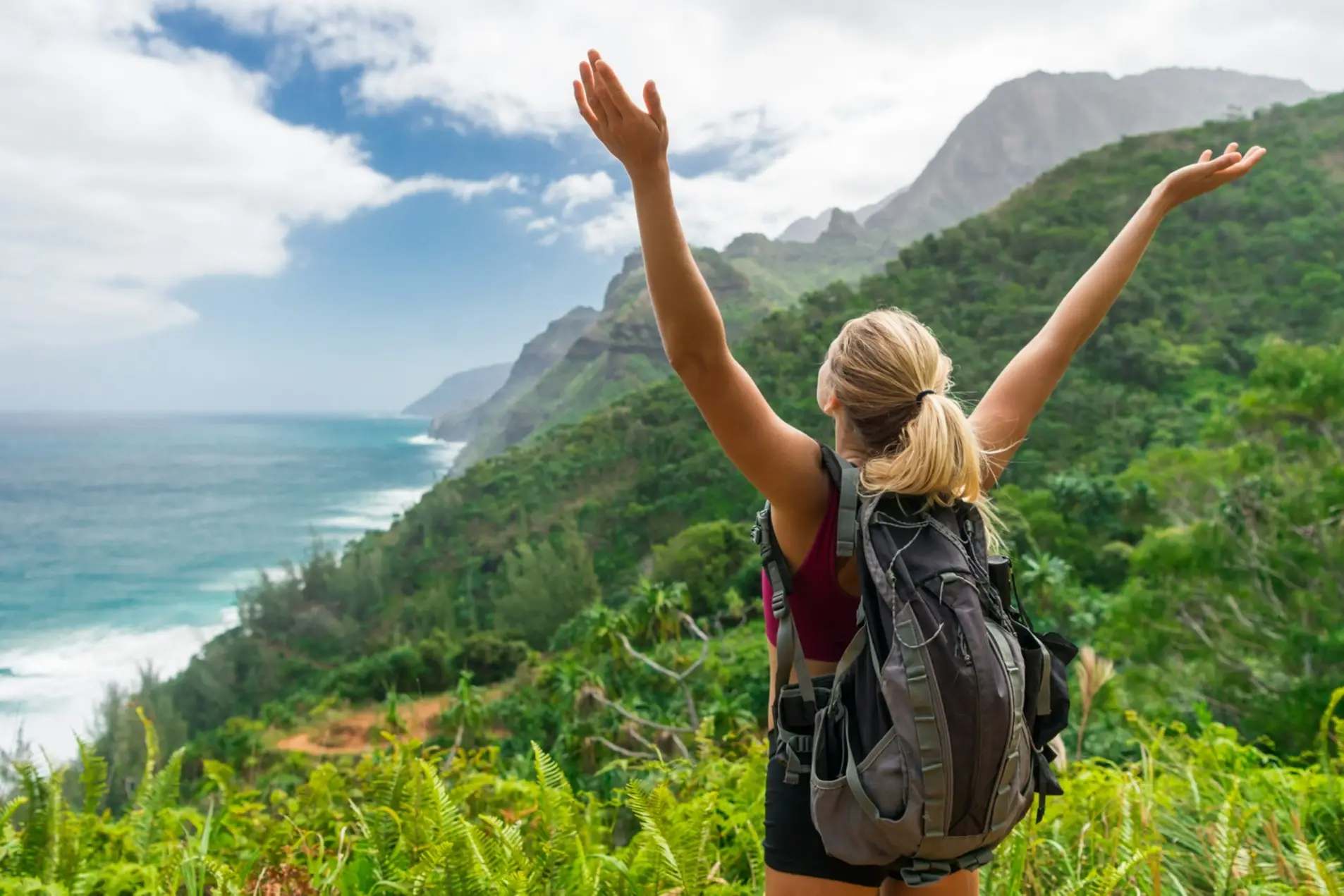 USA, Hawaii, Wandern Eine junge Wanderin mit erhobenen Armen schaut auf den Strand von Hawaii.