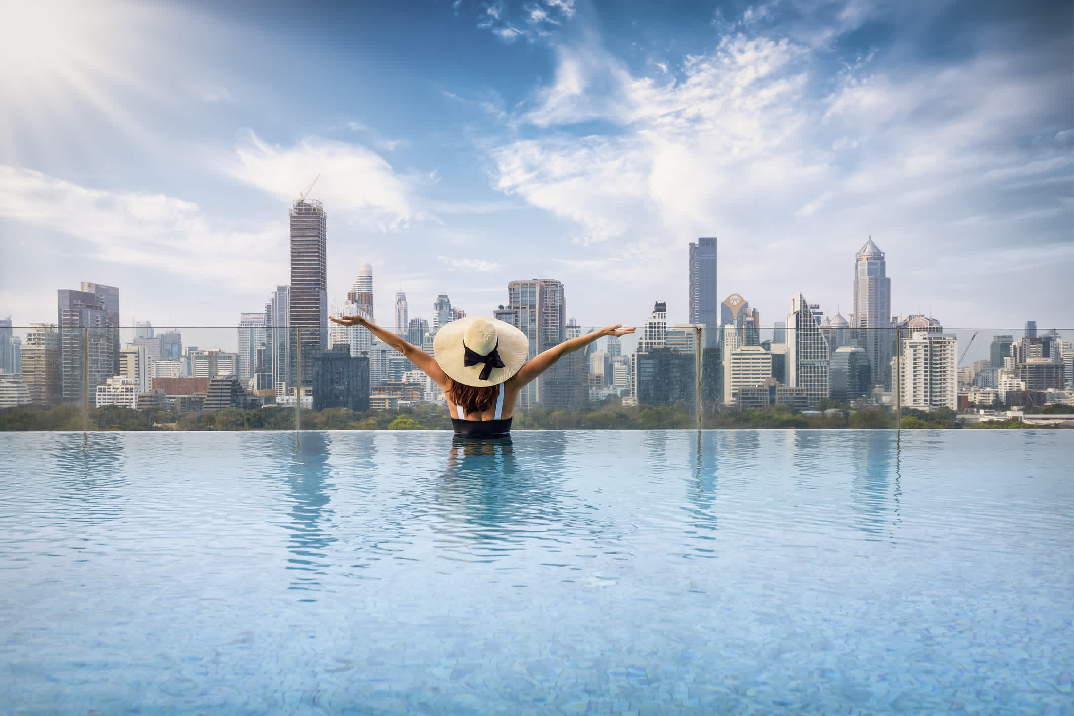 Eine Frau in einem Swimmingpool vor der Skyline von Bangkok, Thailand. 