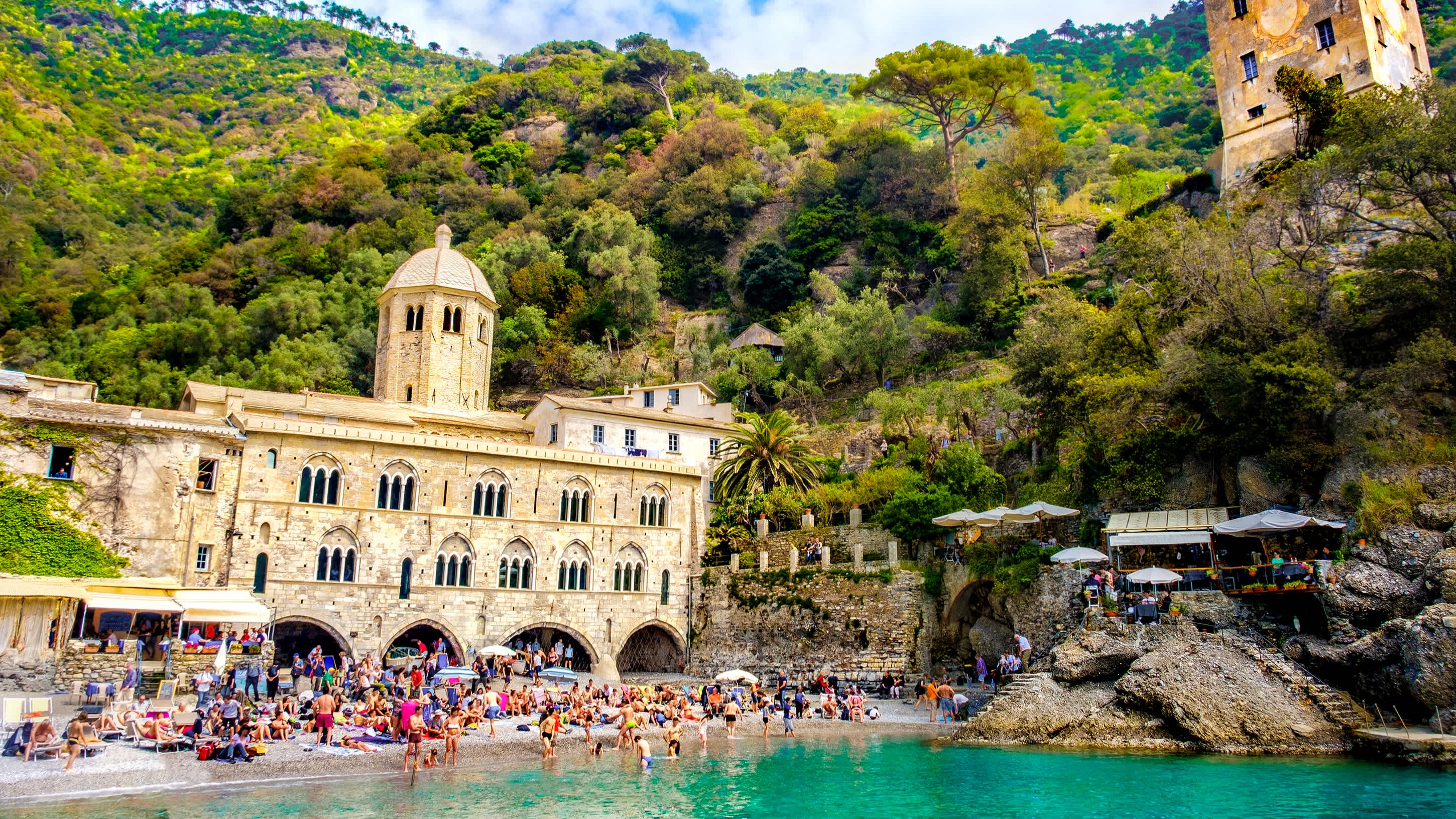 Personnes sur la plage entre Portofino et Camogli en Italie avec un abbaye médiéval entouré de végétation en arrière-plan