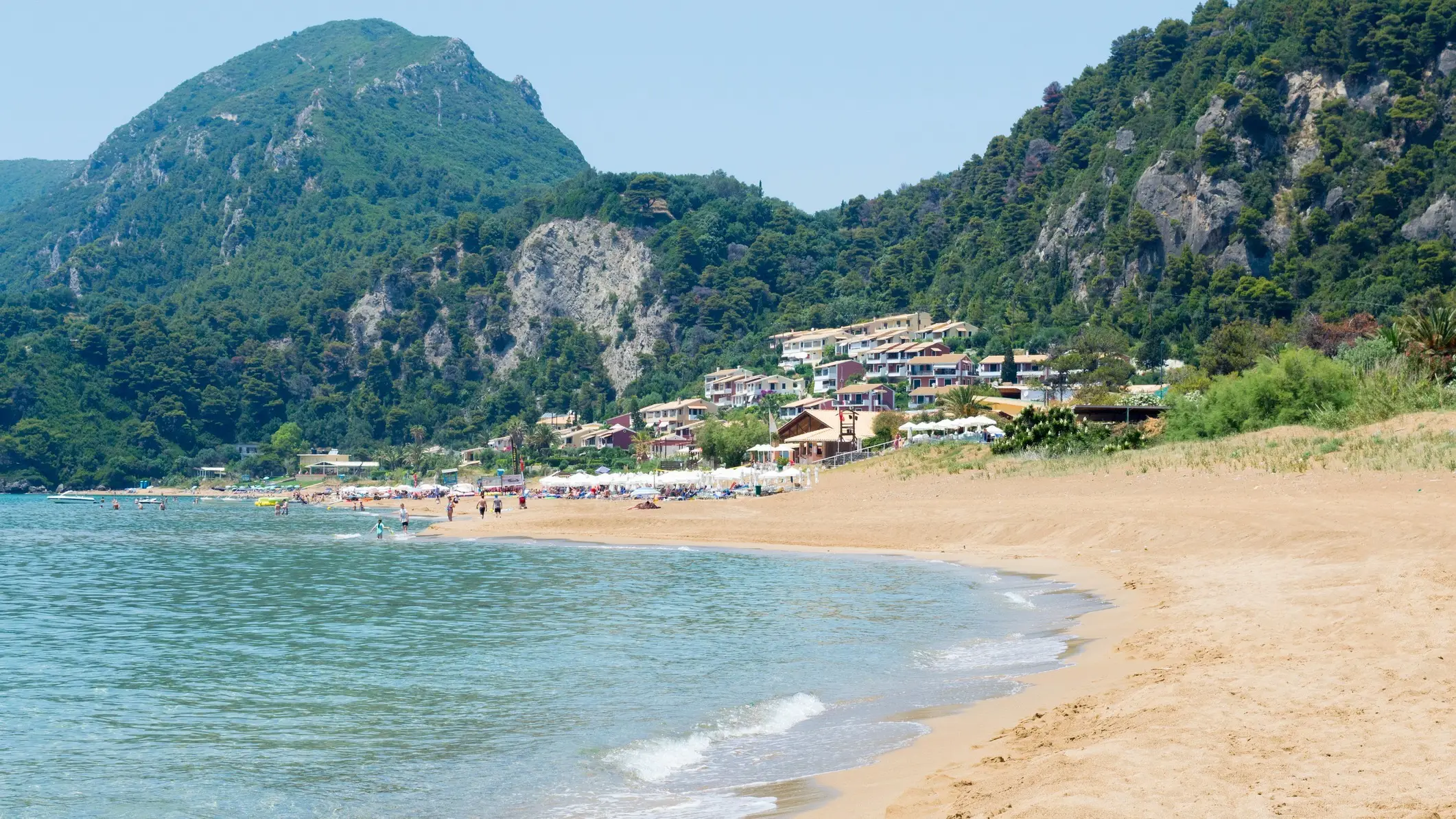 Griechenland, Korfu, Glyfada Beach Der Glyfada Beach auf Korfu, Griechenland mit massiven Bergen im Hintergrund bei Sonnenschein.
