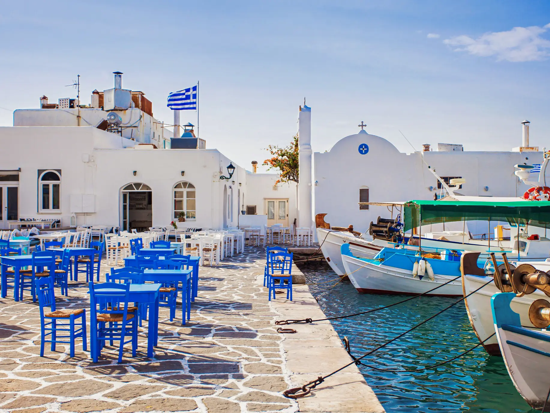 Grèce, Cyclades, Paros, Noussa Petite place sur le port avec des tables et des chaises peintes en bleu et blanc devant des maisons blanches