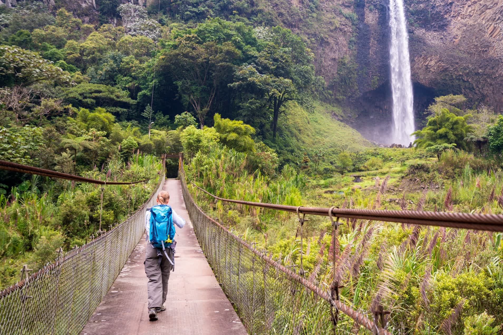 Une voyageuse traversant un pont sur le chemin de la cascade de Bridal Schleier en Équateur.