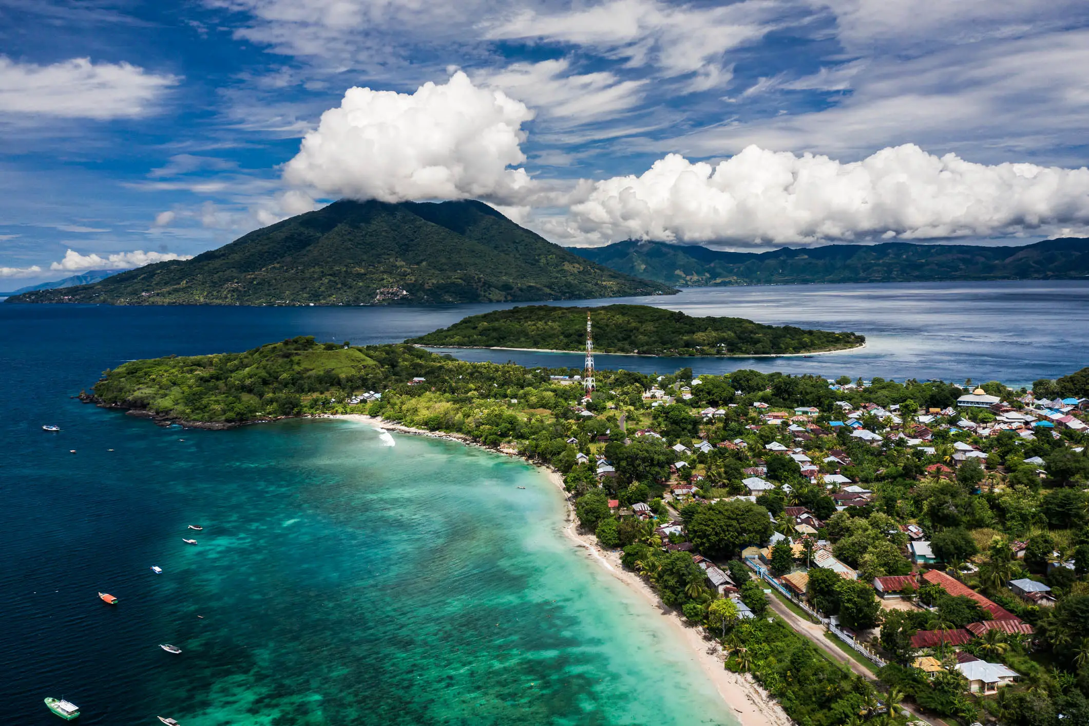 Vue aérienne prise par un drone de la côte de l'archipel de l'île d'Alor, dans la province de Timor, à l'est de l'Indonésie, avec une plage de sable blanc, des récifs coralliens et un volcan surplombant la baie.