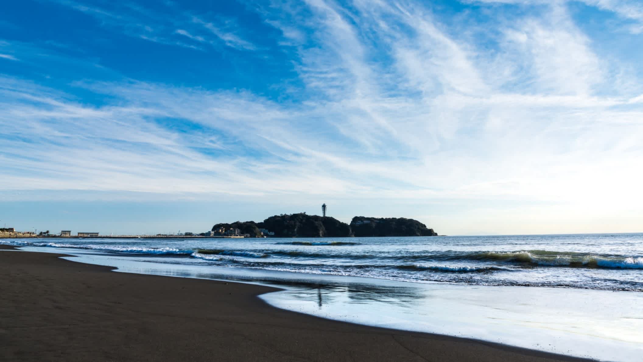 Petites vagues au bord d'une plage d'Enoshima au Japon avec un rocher en arrière-plan.