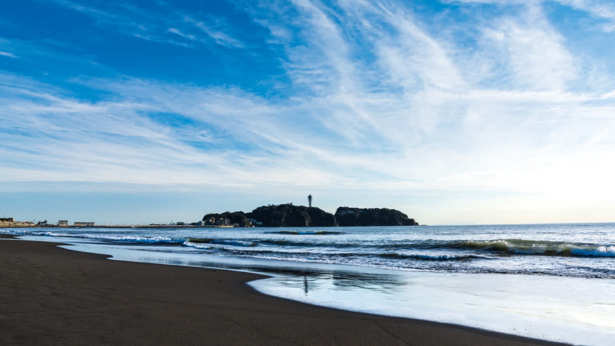 Flaches Wasser bei Ebbe am Strand Enoshima, Kakinuma, Japan und strahlend blauer Himmel mit Blick auf eine vorgelagerte Insel.