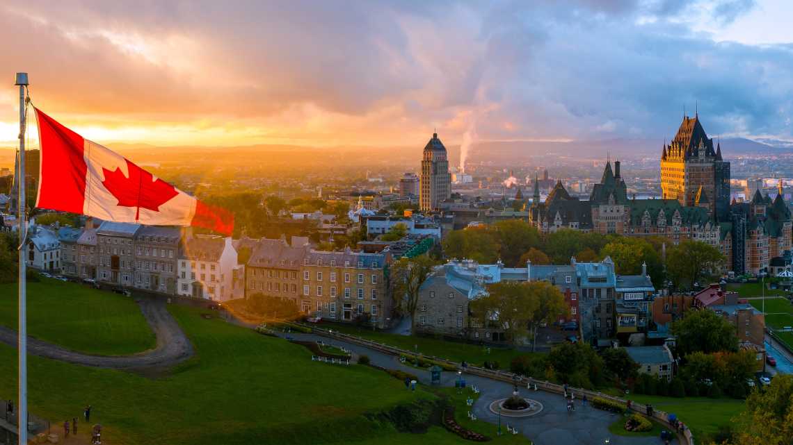 Panoramablick auf die Altstadt von Quebec, Kanada. Auf der linken Seite des Bildes ist eine kanadische Flagge vor einem wunderschönen goldenen Sonnenuntergang zu sehen. 