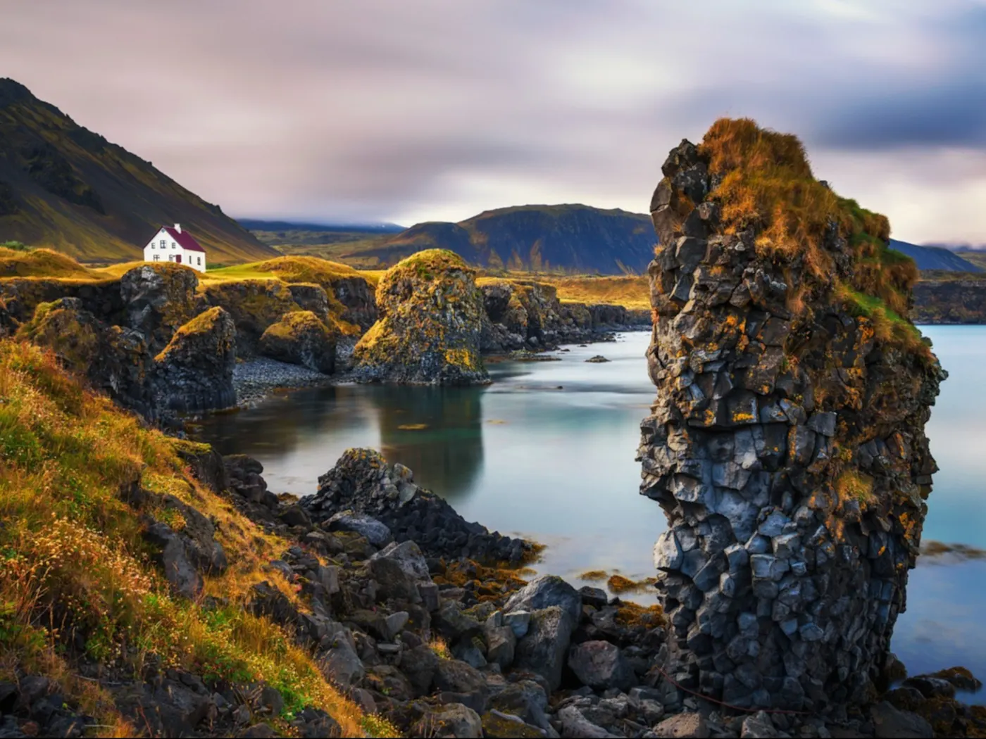 Island Halbinsel Snaefellsnes Ein Blick auf die zerklüftete Küstenlinie mit einem einsamen Haus. Herbstfarben mit schneebedeckten Bergen im Hintergrund. Halbinsel Snaefellsnes in Island