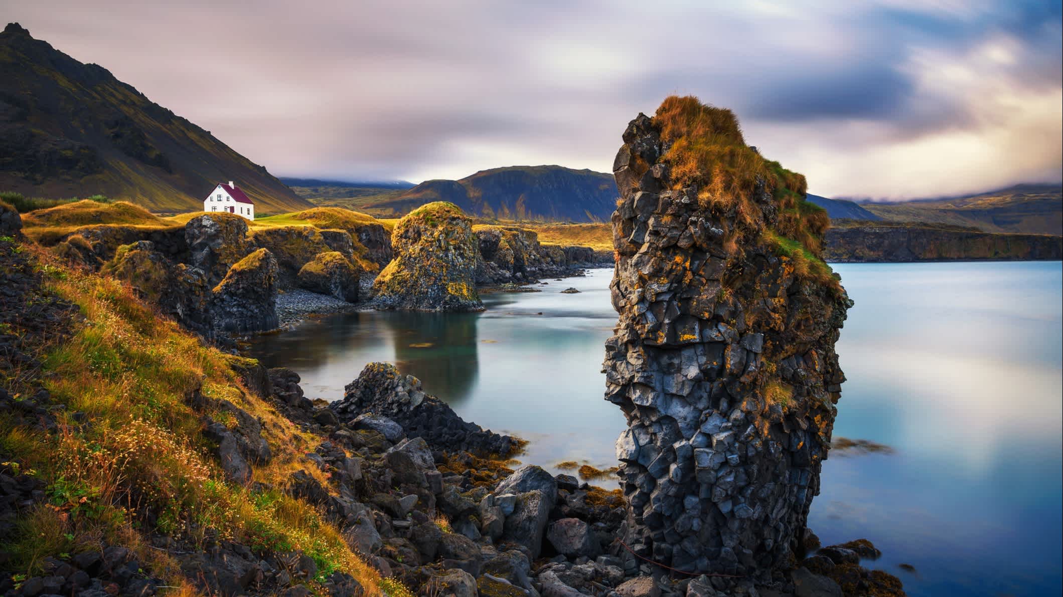 Une vue de la côte déchiquetée avec une maison isolée. Couleurs d'automne avec des montagnes enneigées en arrière-plan. Péninsule de Snaefellsnes en Islande.