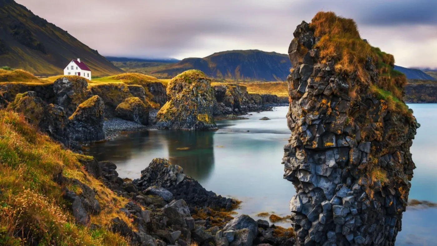 Une vue de la côte déchiquetée avec une maison isolée. Couleurs d'automne avec des montagnes enneigées en arrière-plan. Péninsule de Snaefellsnes en Islande