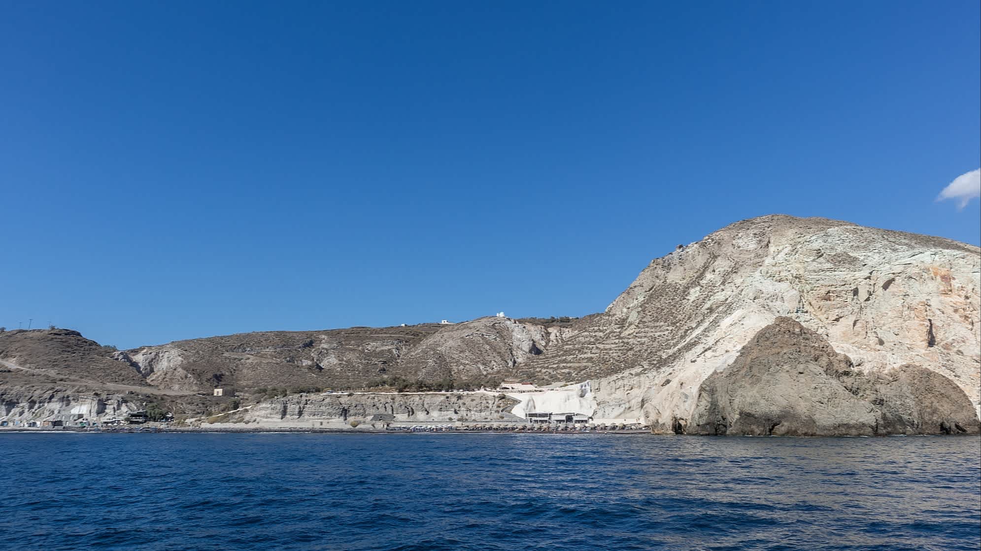 Blick vom Meer auf die weißen Klippen am Strand White Beach auf Santorini, Griechenland bei Sonnenschein.