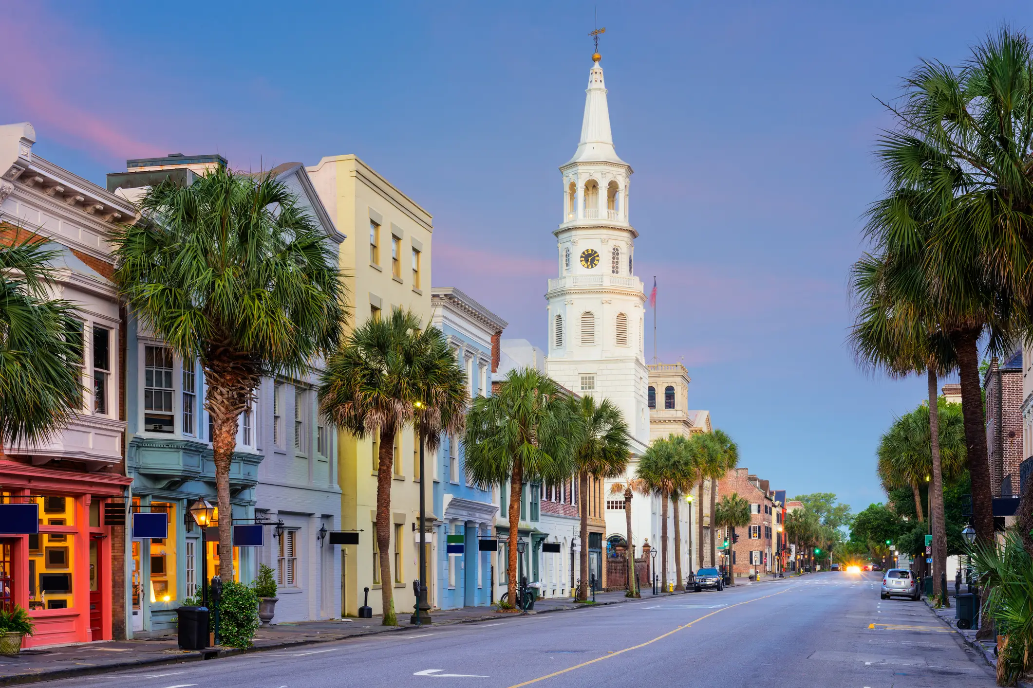 Historische Straße in Charleston mit bunten Gebäuden, weißem Kirchturm und Palmen unter violett-blauem Abendhimmel.
