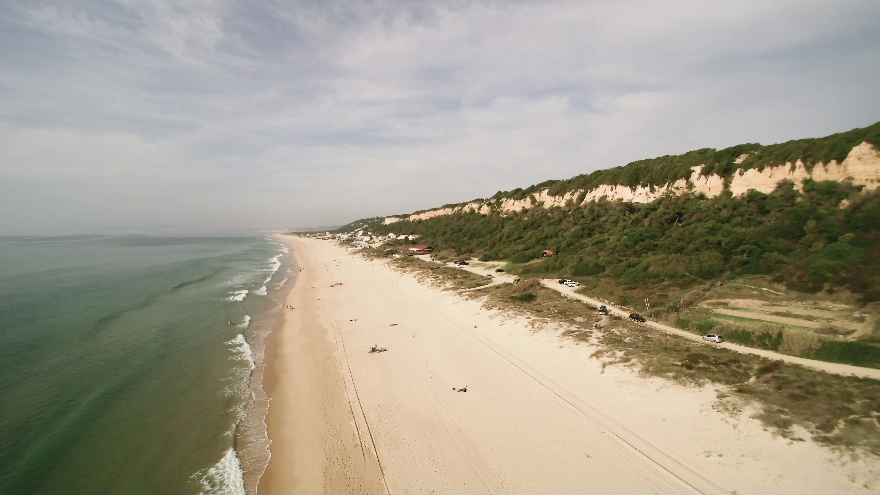 Praia da Fonte da Telha, Portugal Der lange Sandstrand von Praia da Fonte da Telha, Portugal mit grünen Dünen bei bewölktem Wetter.