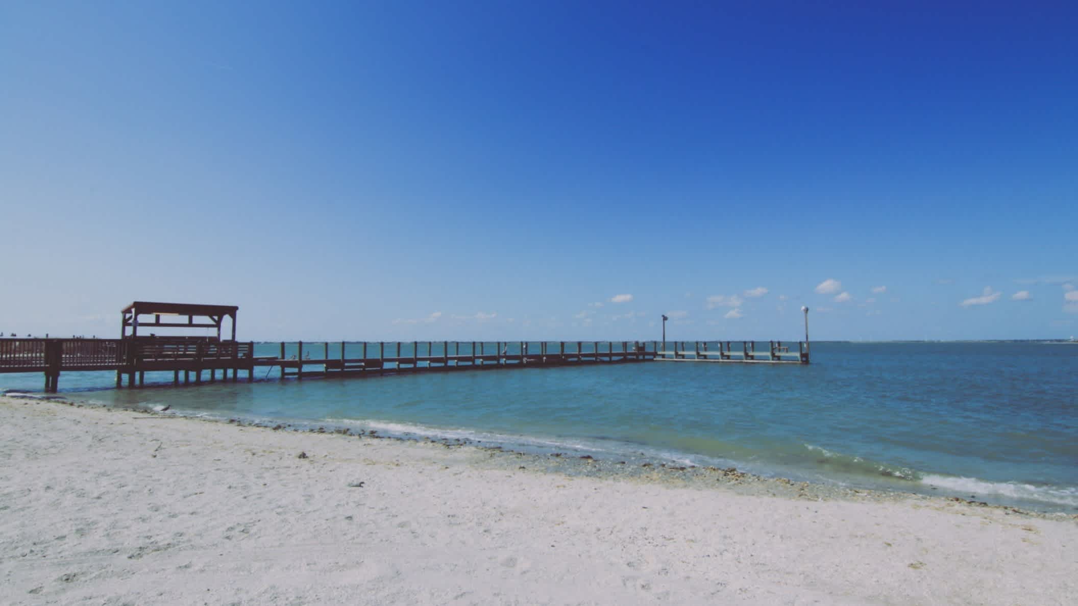 Der Strand IB Magee Beach, Port Aransas, Texas, USA bei blauem Himmel und Sonne mit Blick auf einen Steg.