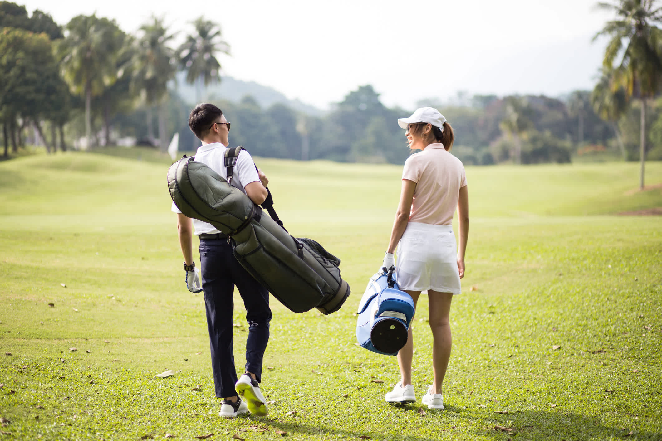 Asiatisches Paar zu Fuß zusammen auf dem Golfplatz mit ihren Golftaschen.

