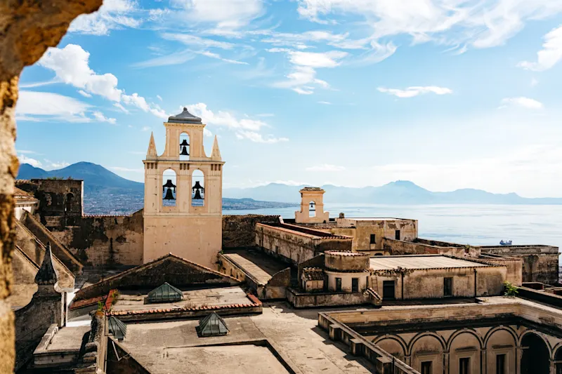 Italy, Naples, Bell Tower Historic monastery with bell tower on the Italian coast, view of mountains and sea under blue sky.