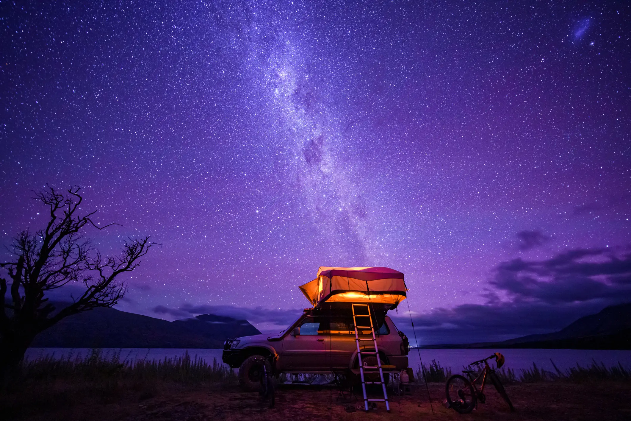 Voiture avec tente sur le toit devant un lac sous un beau ciel étoilé, Nouvelle-Zélande