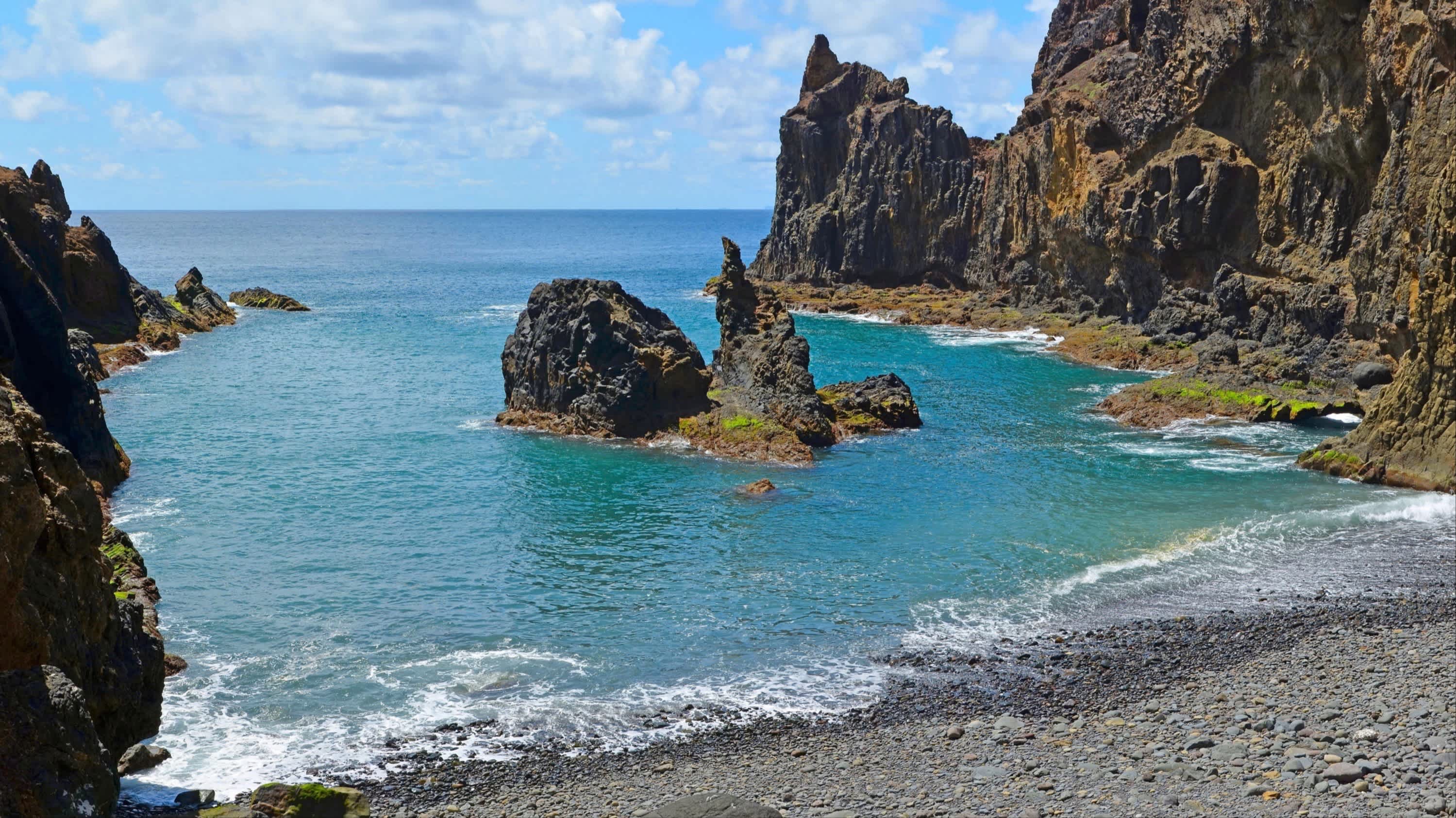 Kleiner grauer Kieselstrand umgeben von Felsen am Praia Porto Santo, Porto Santo, Madeira, Portugal.