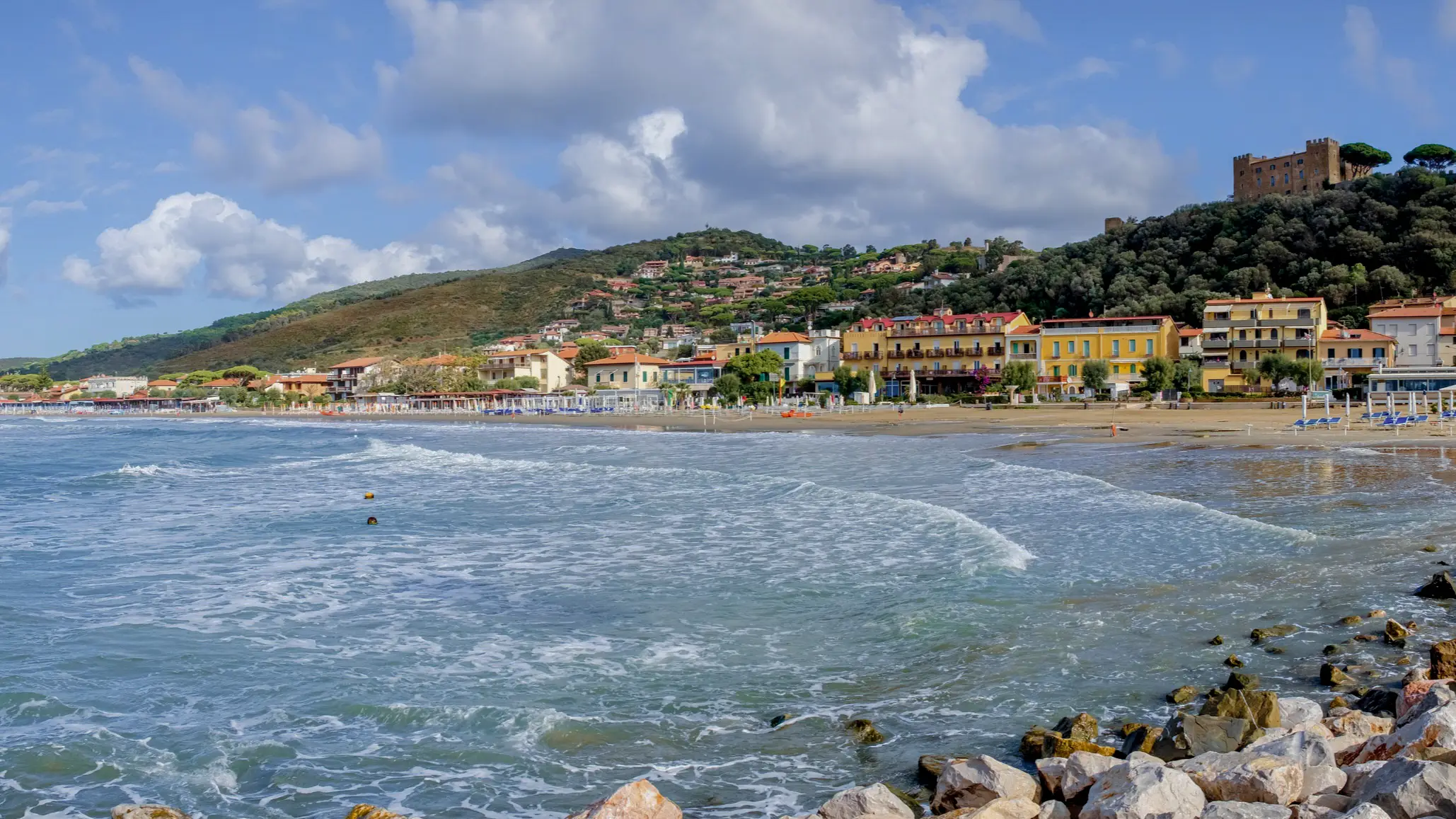 Italien, Toskana, Castiglione della Pescaia Meereslandschaft in Castiglione della Pescaia, Toskana, Italien mit Häusern am Rand des Strandes und Bergen im Hintergrund.