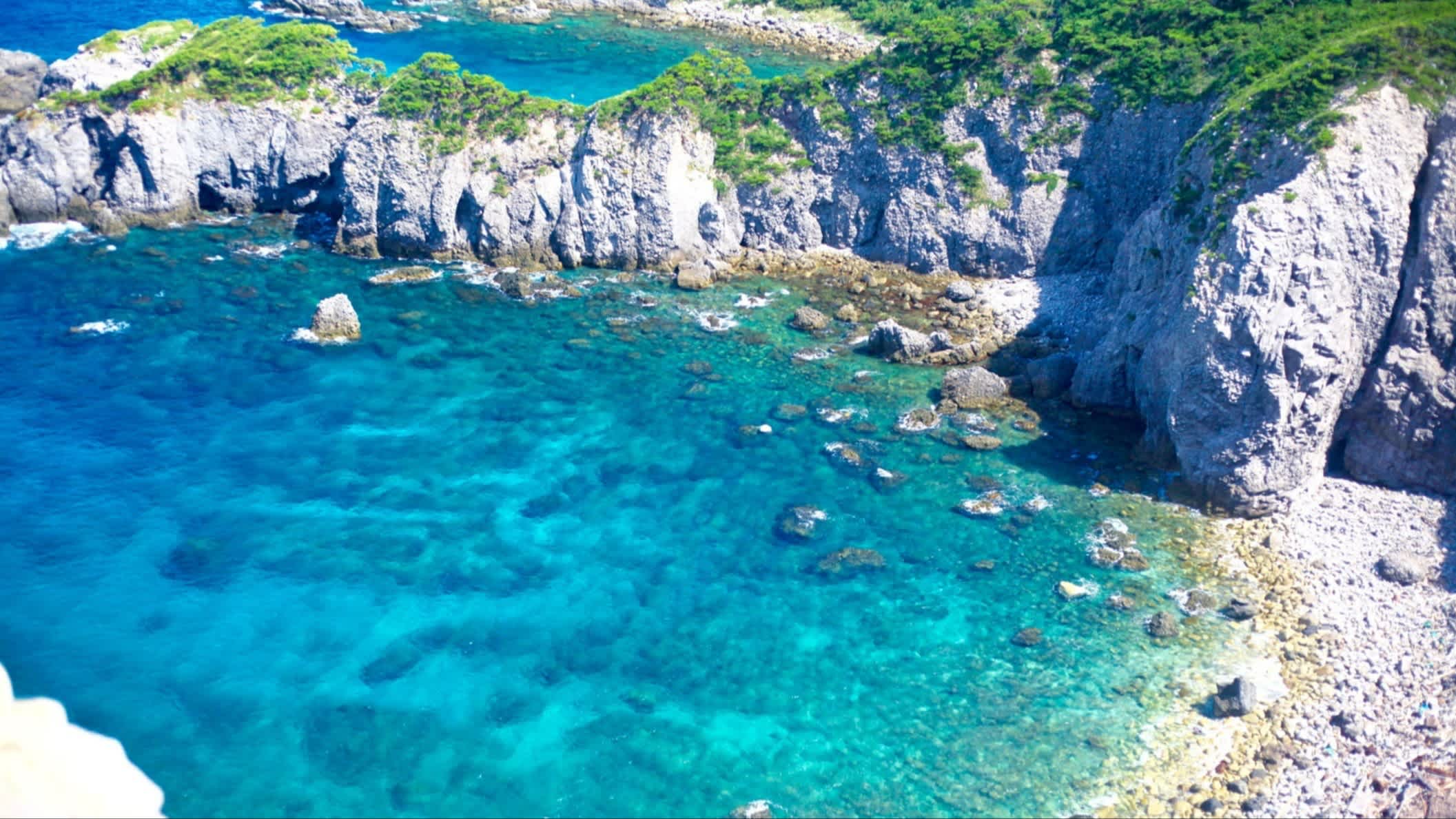 Blick auf die kleine Bucht von Shikinejima, Niijima-mura, Japan mit türkisblauem Wasser und Felsen.