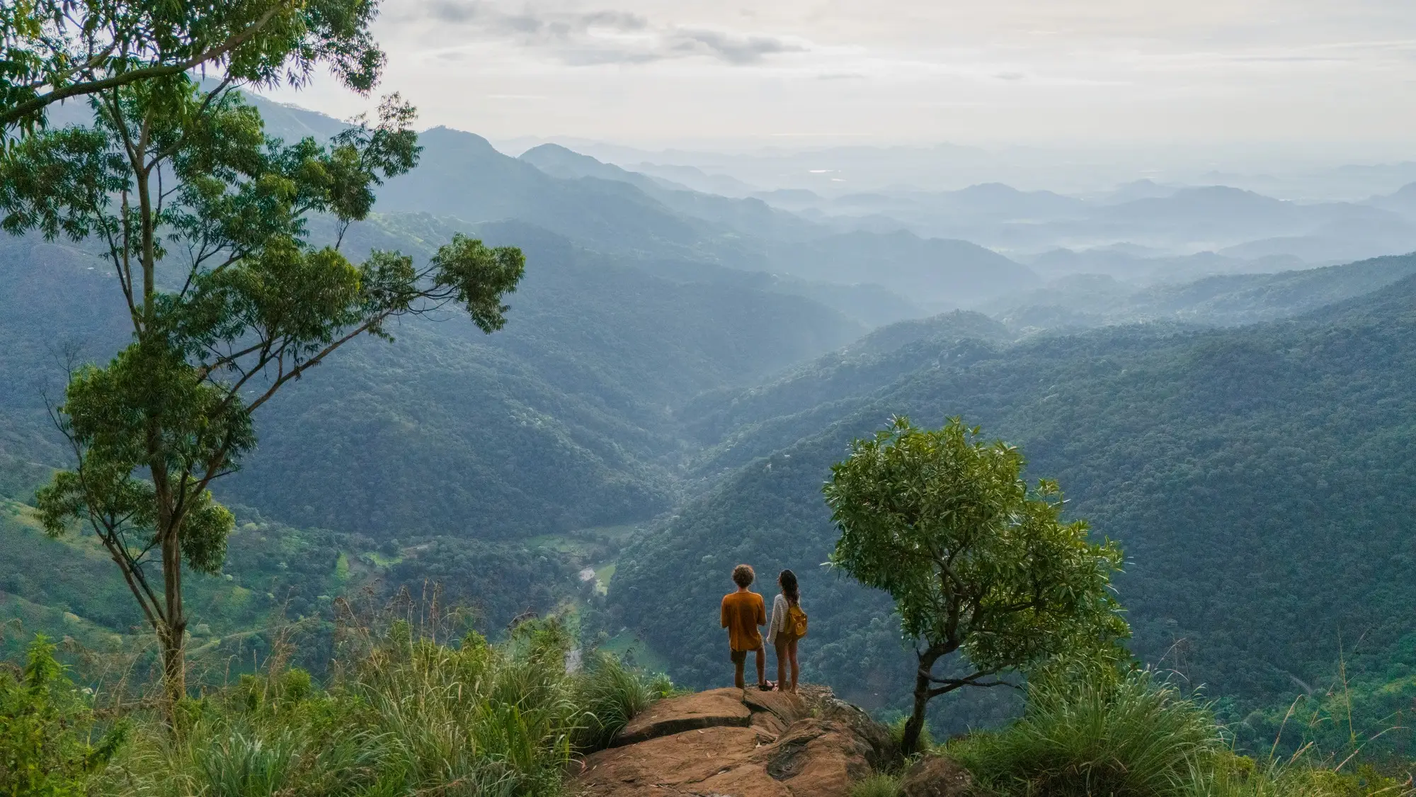 Vue aérienne d'un homme et d'une femme debout sur le rocher d'Ella, contemplant les collines verdoyantes