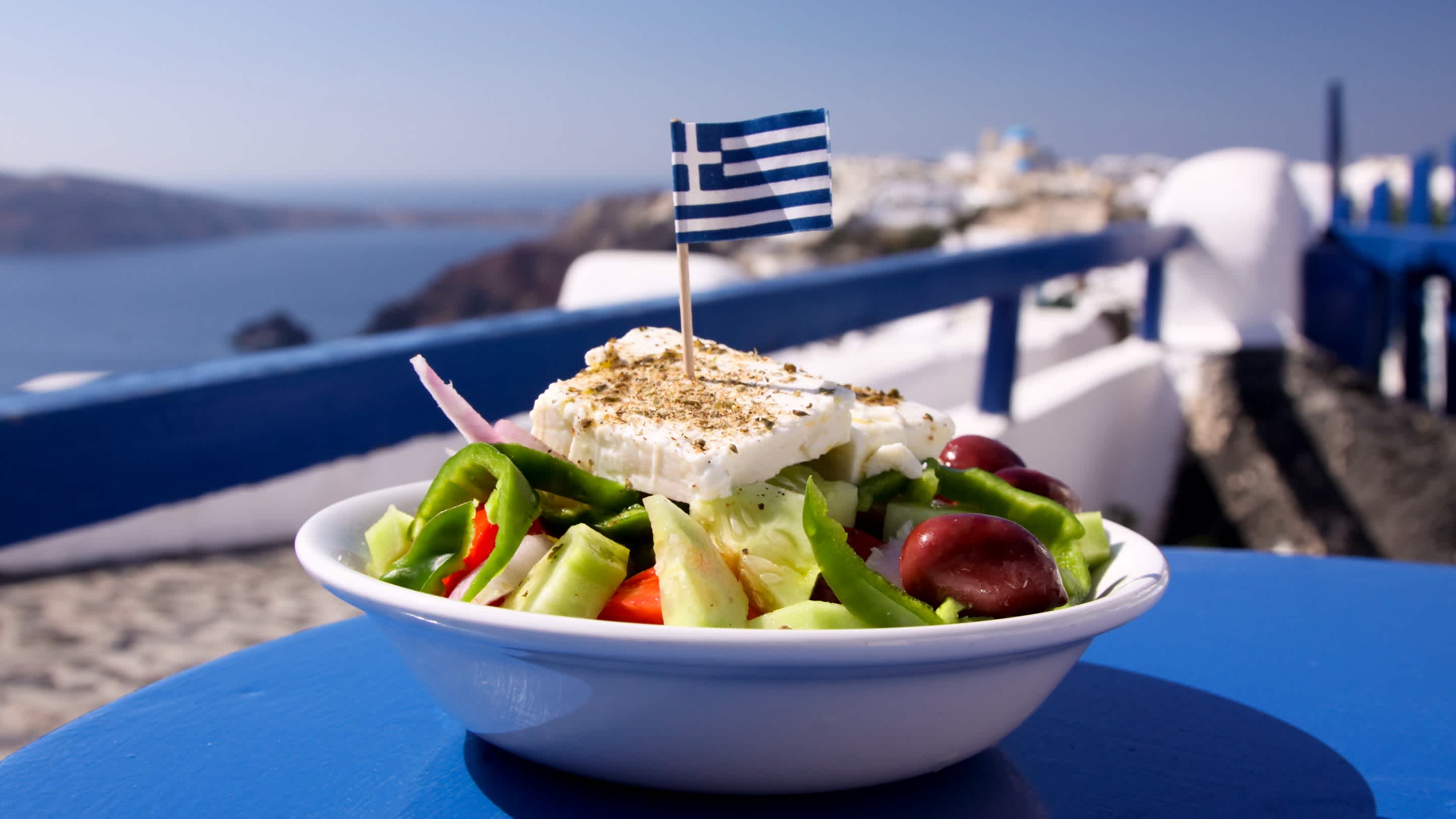 Ein griechischer Salat mit Fetakäse, gekrönt mit einer griechischen Flagge, in Oia, Santorini

