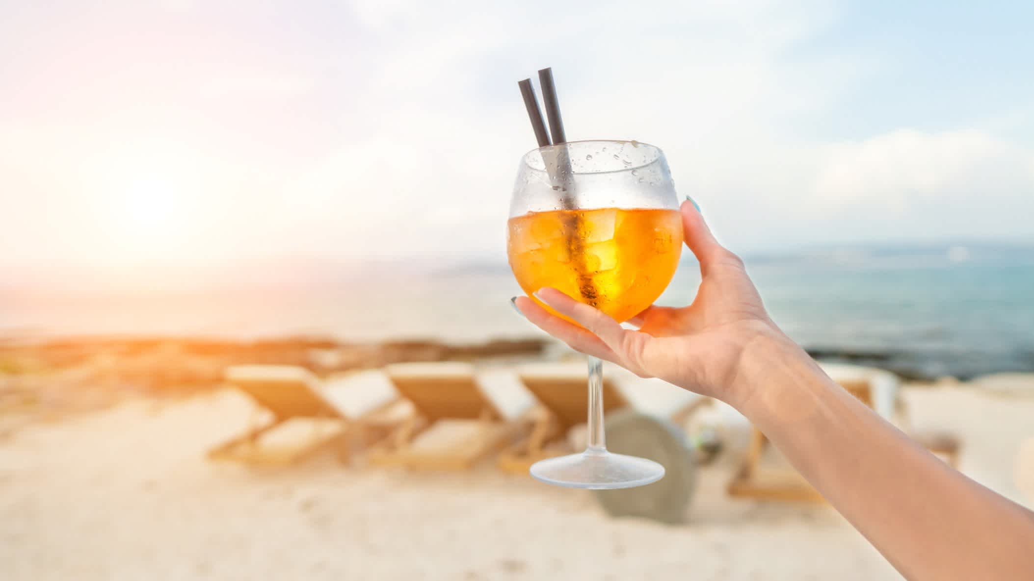 Eine Frau mit einem Spritz Cocktail bei auf den Strand bei Sonnenuntergang 