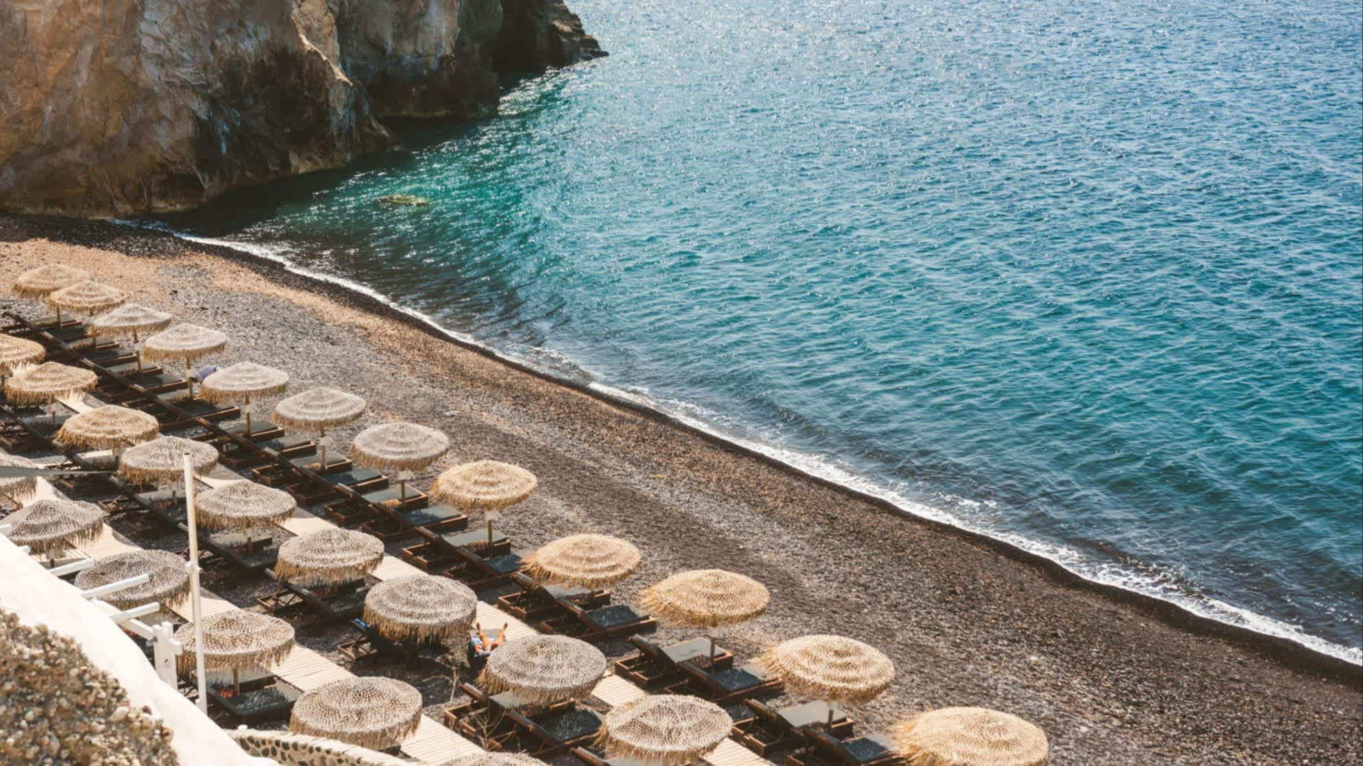 Blick zum Mesa Pigadia Strand, Santorini, Griechenland mit Sonnenschirmen und Meer.