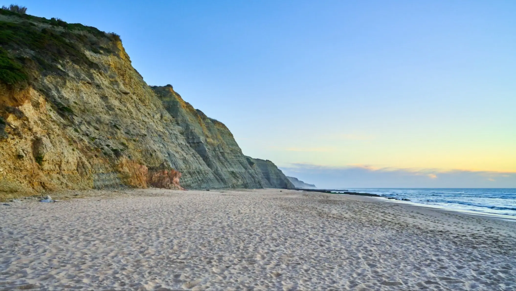 Vue du sable entourée de falaises au coucher du soleil sur la plage de Magoito au Portugal