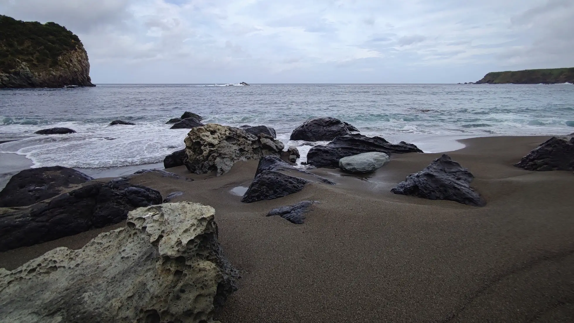 Portugal, Azoren, Corvo Schwarzer Sandstrand auf der Vulkaninsel Corvo, Azoren, Portugal bei bewölktem Wetter und mit Felsen im Bild.