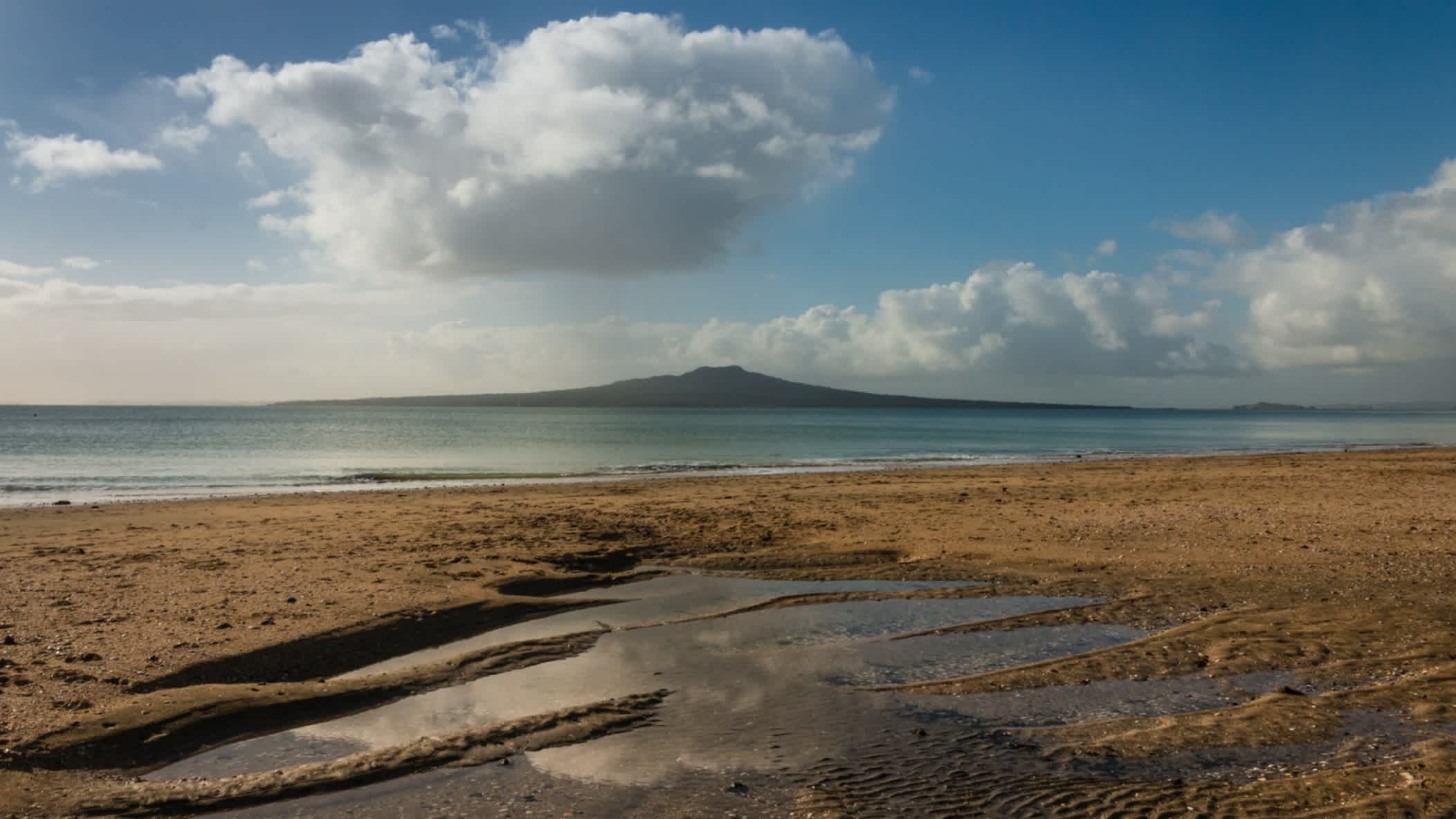 Takapuna Strand bei Ebbe, Auckland, Neuseeland und bei Sonnenschein mit Blick auf eine vorgelagerte Insel.
