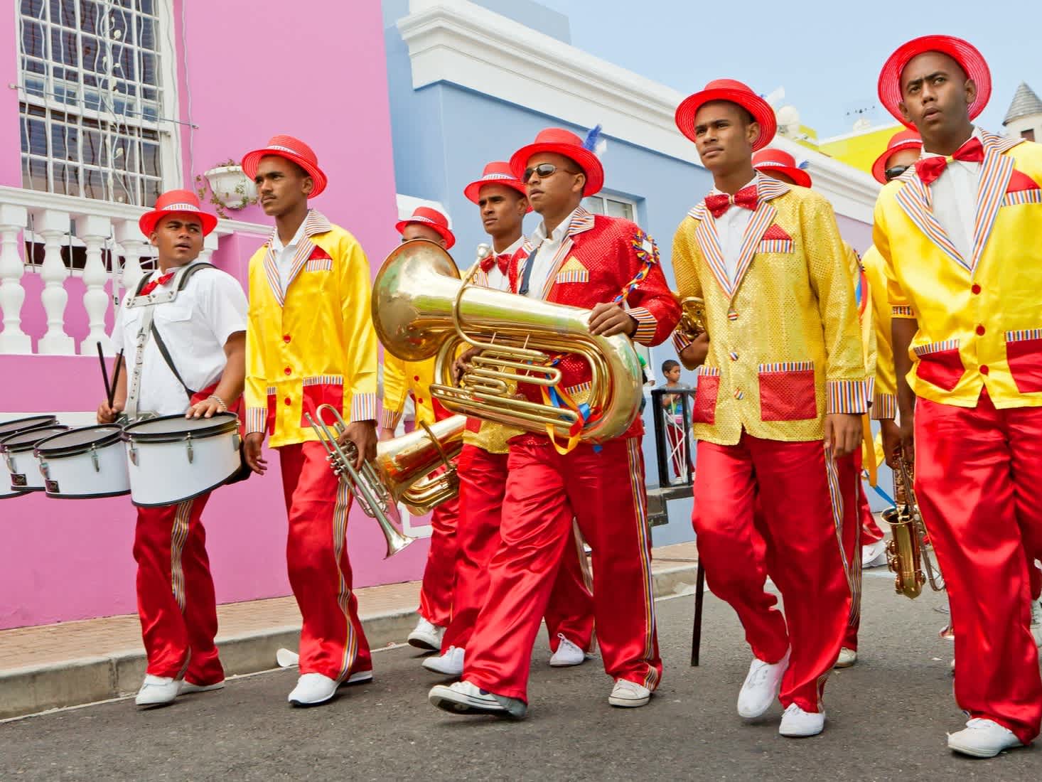 Des musiciens en costumes colorés devant une façade de maison multicolore