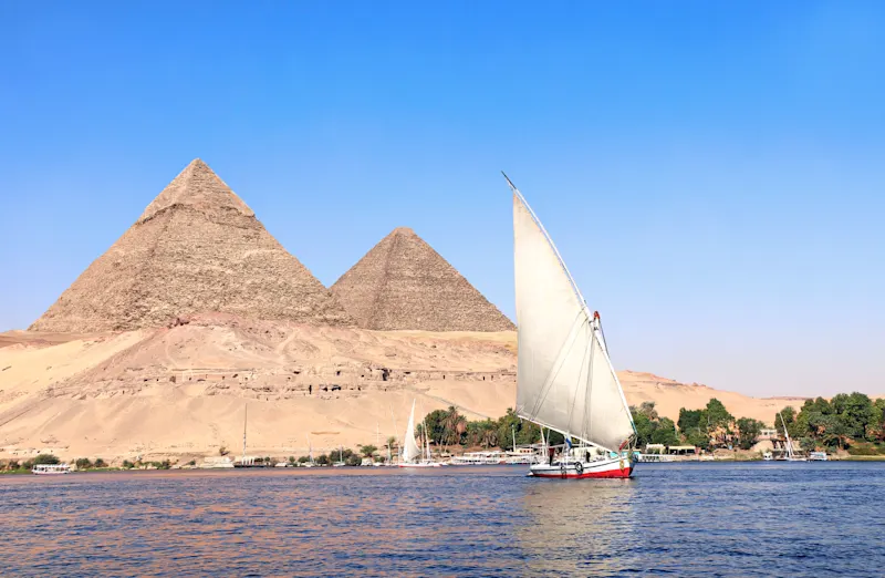 Traditionelles Segelboot auf dem Nil vor den Pyramiden von Gizeh unter klarem blauem Himmel in Ägypten.