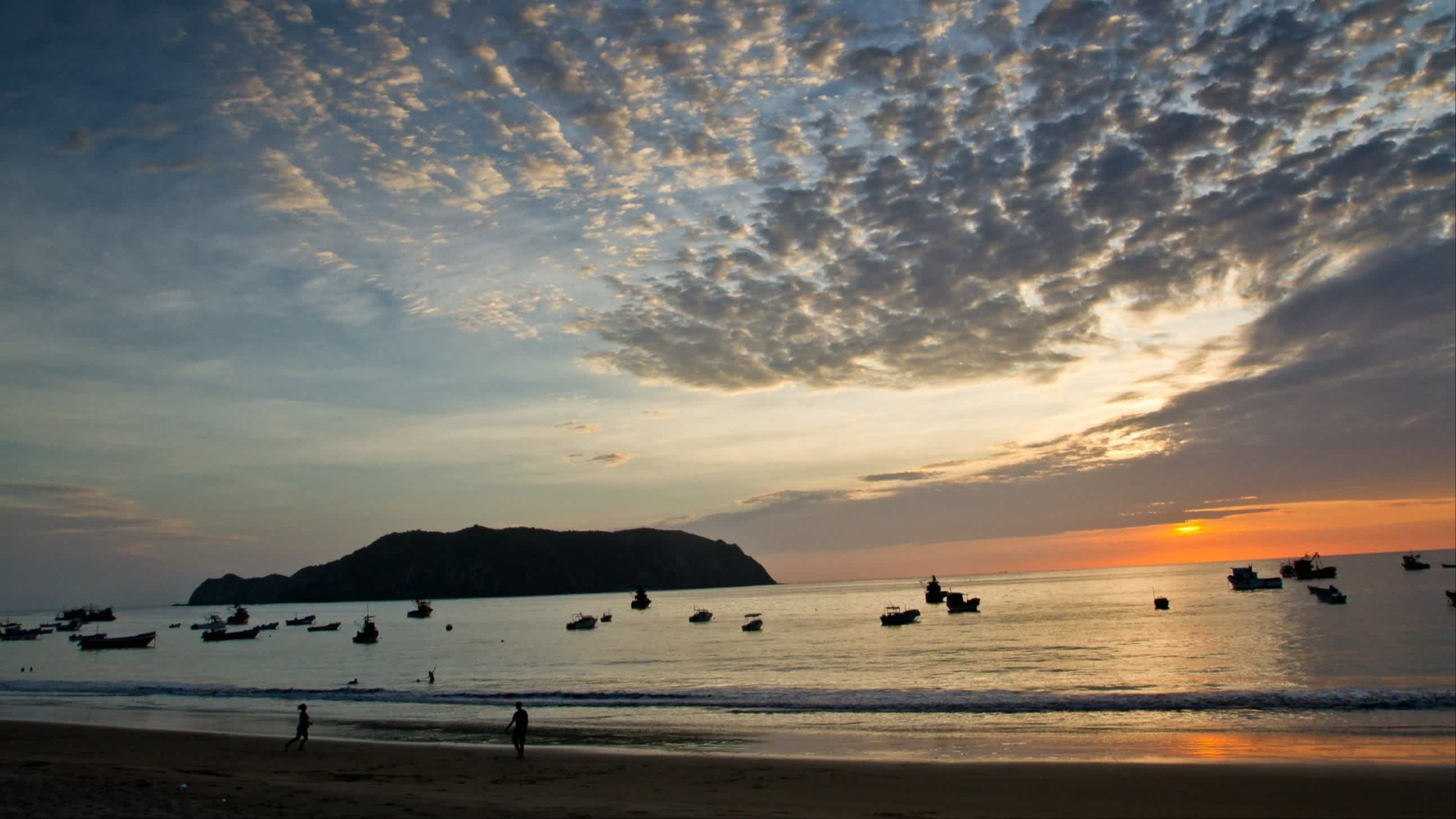 Der Strand von Salango, Provinz Manabí, Ecuador bei Sonnenuntergang mit Blick auf die Bucht und einer  vorgelagerten Insel sowie Booten im Wasser.