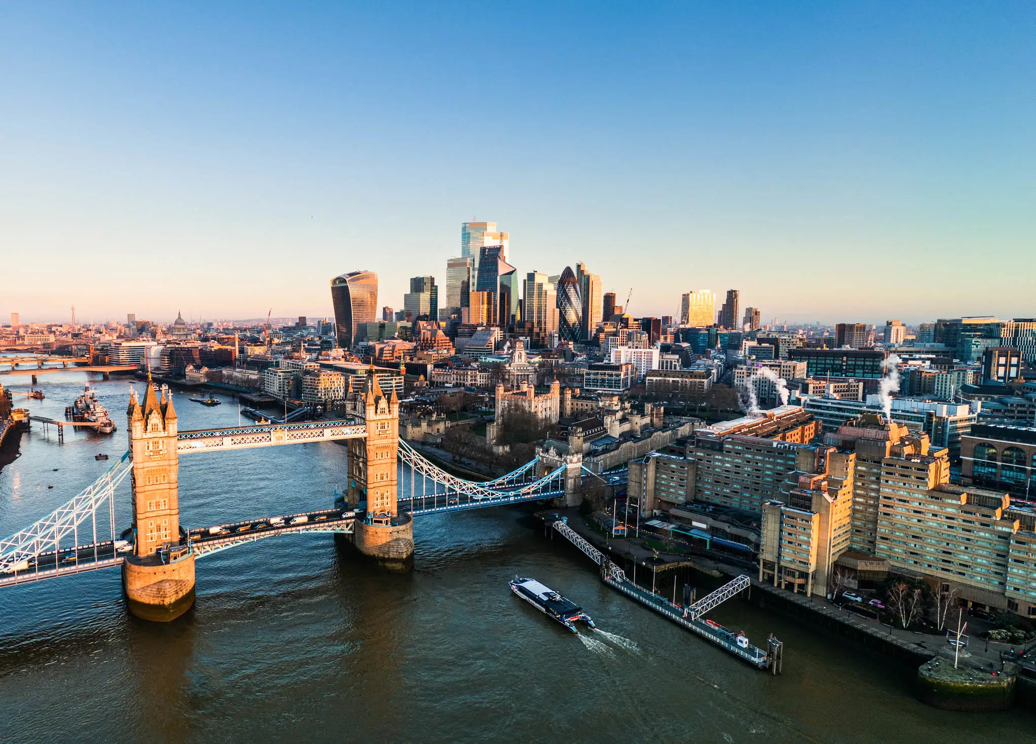 Luftaufnahme von London mit Tower Bridge und Themse im Vordergrund, Skyline mit Wolkenkratzern im goldenen Abendlicht.