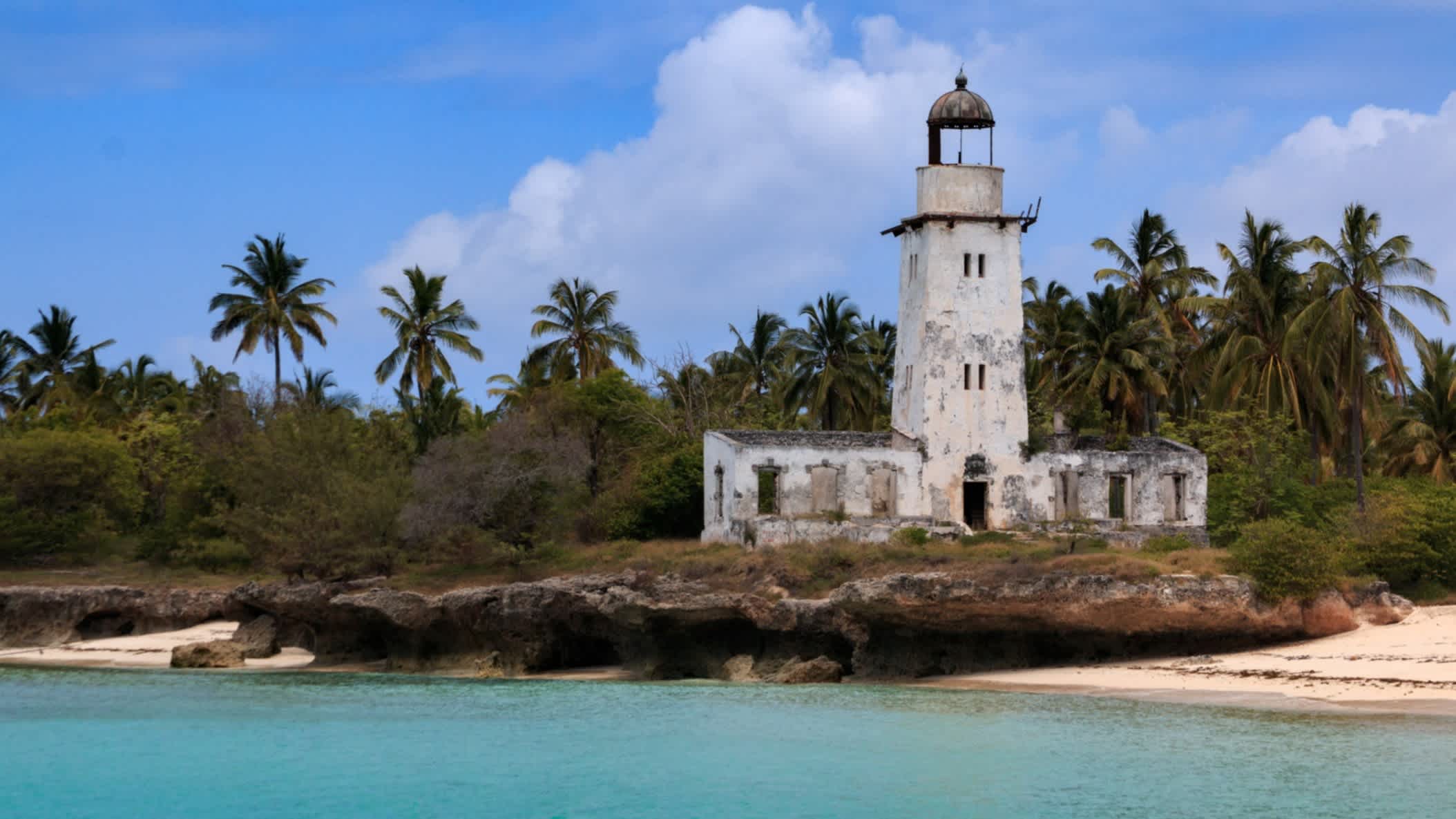 Der Leuchtturm auf der Insel Fanjove im azurblauen Indischen Ozean und mit Palmen im Hintergrund vor der Küste Tansanias.
