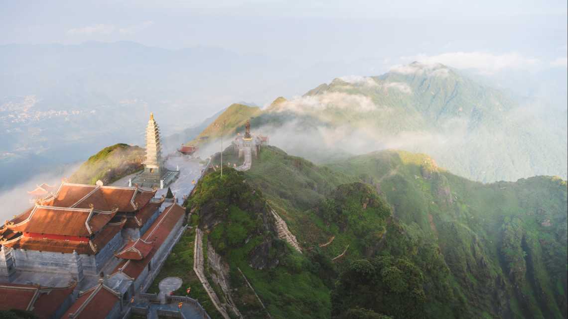 Neblige weite Landschaft des Fansipan-Bergs mit einem buddhistischen Tempel, Vietnam.