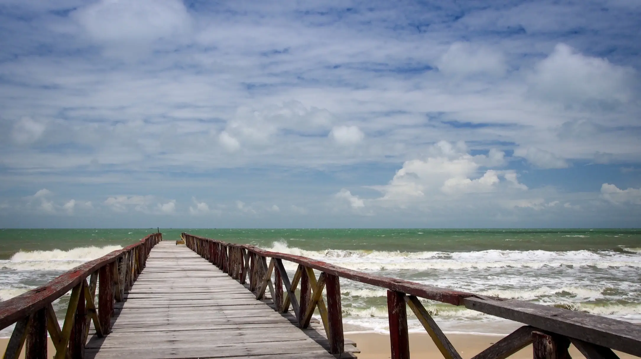 Koh Thmei Strand im Ream National Park, Kambodscha mit Blick auf einen Steg sowie tosenden Wellen im Meer und bewölktem Himmel.