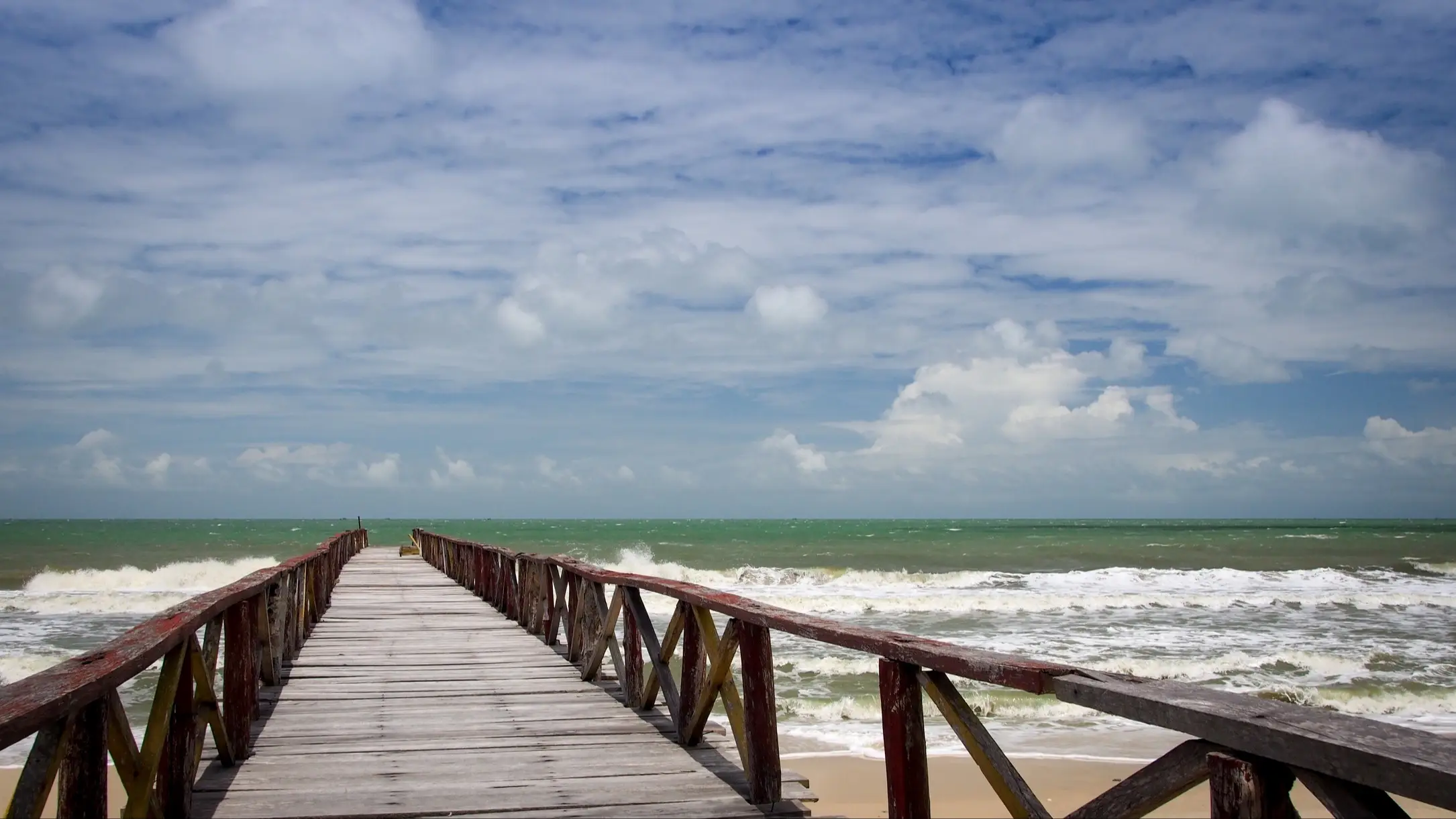 Koh Thmei, Ream National Park, Kambodscha Koh Thmei Strand im Ream National Park, Kambodscha mit Blick auf einen Steg sowie tosenden Wellen im Meer und bewölktem Himmel.